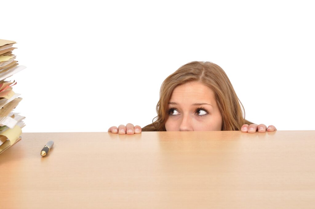 Junge Frau versteckt sich hinter dem Schreibtisch